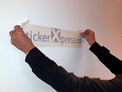 Twee handen zetten de belettering met schilderstape vast op een witte muur