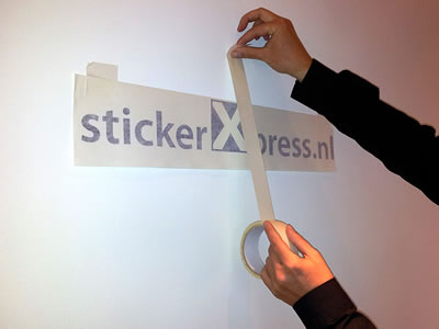 Een strook schilderstape gaat verticaal over het midden van de belettering