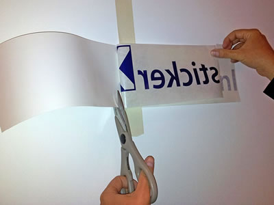 Een schaar knipt het rugpapier langs de scharniertape af