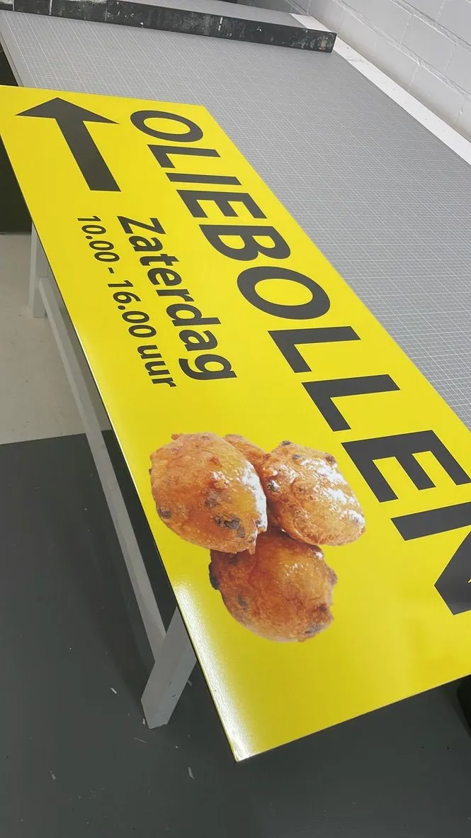 Geel bord met een pijl en oliebollen voor de verkoop op zaterdag