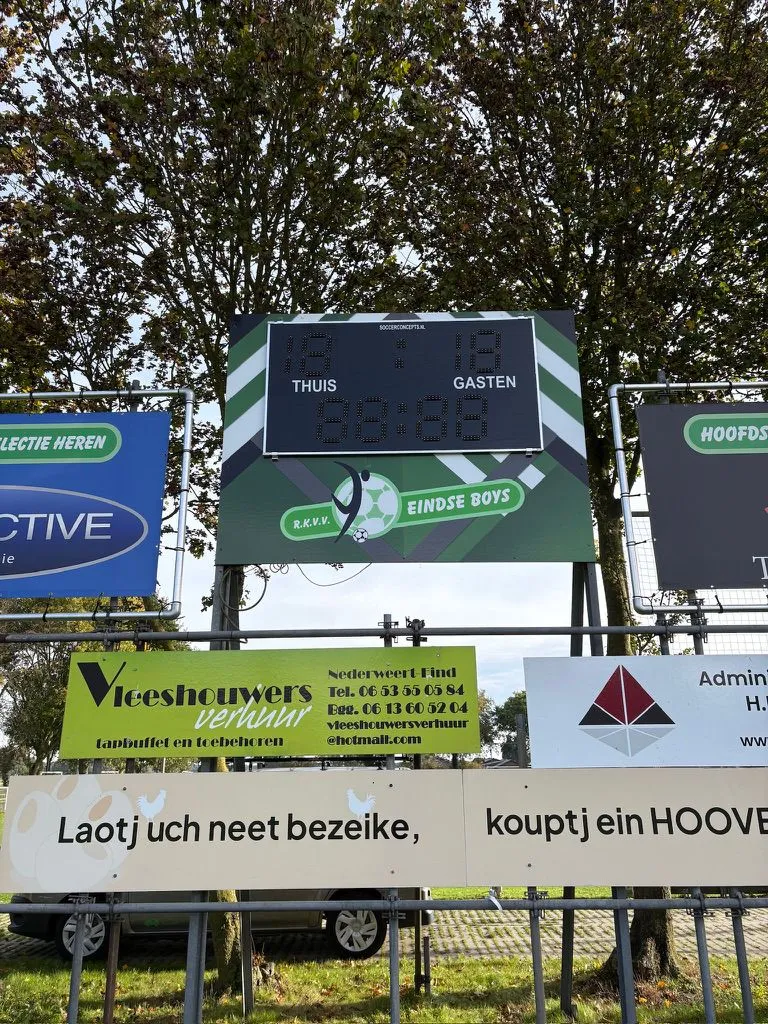 Scorebord en reclameborden van sponsors langs een sportveld
